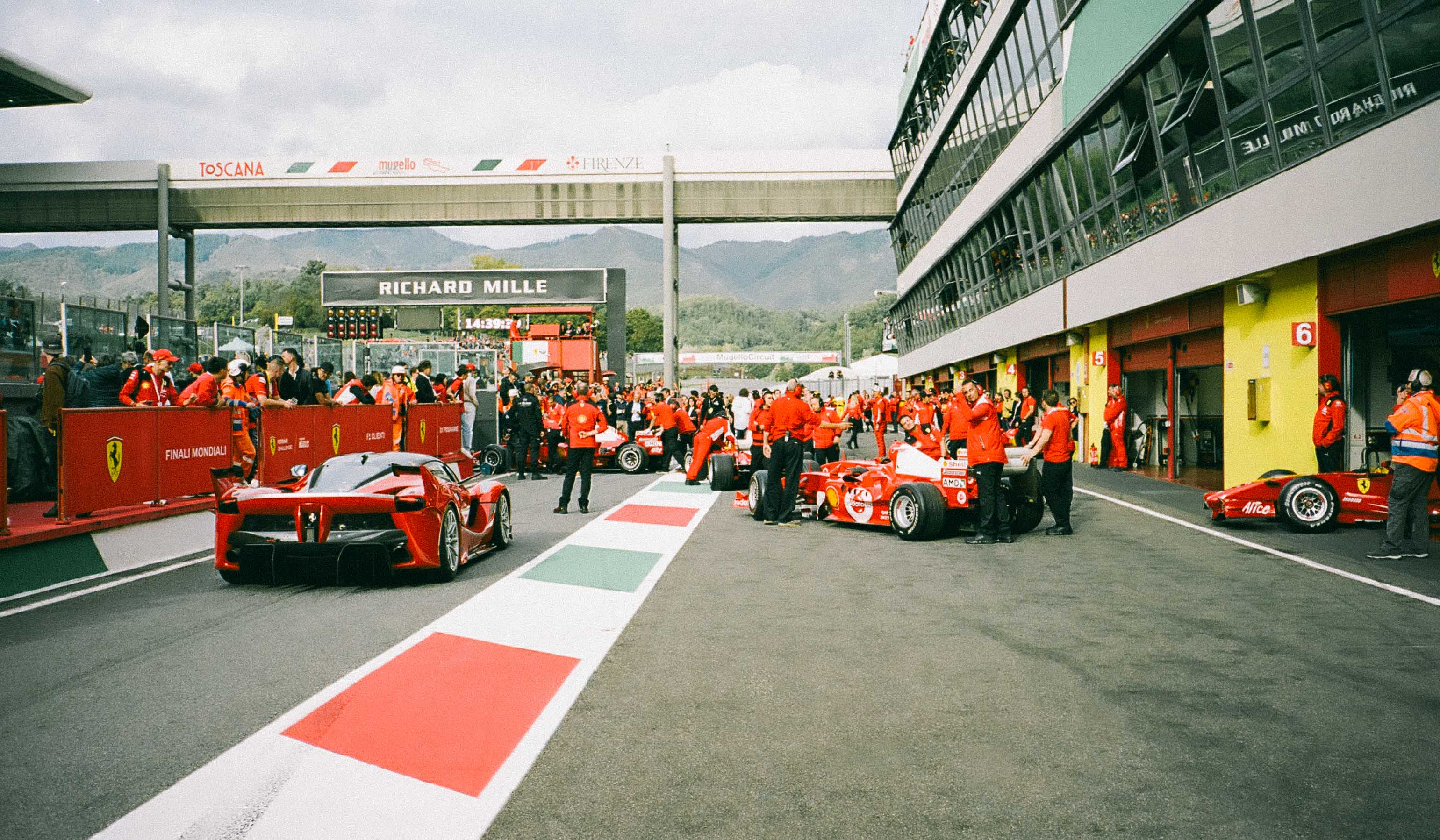 Ferrari racing cars on a track with team members and support staff.